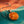 Round orange stone pendant on a silver chain, placed on a teal and orange fabric background.