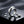 Silver ring and droplets on a glossy black surface, with scattered metallic pebbles.