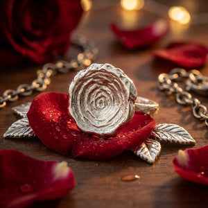 Silver ring on red rose petals, with water droplets and a chain in the background.