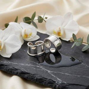 Silver rings on black slate with white orchids and eucalyptus leaves, set on a cream fabric.