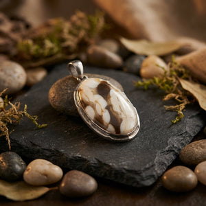Oval pendant with brown and white swirled stone on slate, surrounded by pebbles and moss.