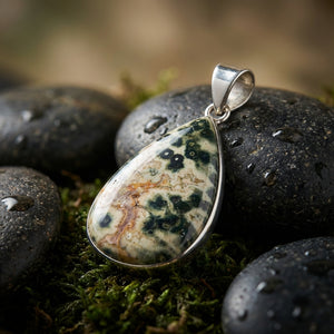 Teardrop-shaped stone pendant with green and beige patterns on wet black stones and moss.