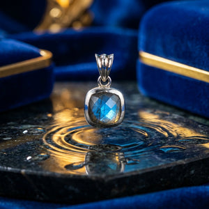 Silver pendant with blue gemstone on reflective surface, surrounded by deep blue velvet cases.