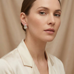 Woman in a cream blouse with silver shell earrings against a soft beige background.