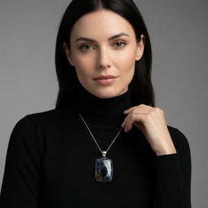 Woman in black turtleneck with dark hair and a large rectangular pendant on a silver chain.