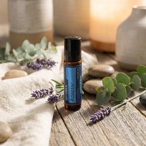 Essential oil bottle with blue label on wood, surrounded by lavender, stones, and eucalyptus leaves.