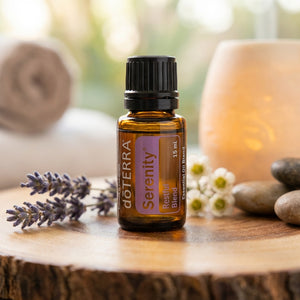 Amber essential oil bottle on a wooden surface, surrounded by lavender, flowers, stones, and a candle.