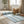 Striped blue rug on wooden floor, wicker basket with towels, books, sandals, and potted plant nearby.
