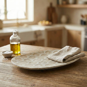 Rustic kitchen scene with a wooden table, glass oil bottle, salt bowl, and textured plate with cloth.
