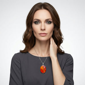 Woman with wavy brown hair, wearing a gray top and an orange pendant necklace, against a gray background.