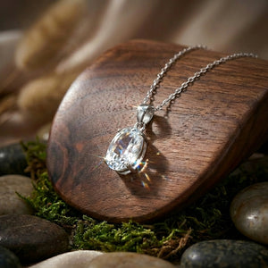 Silver chain necklace with a sparkling crystal pendant on a wooden stand, surrounded by moss and stones.