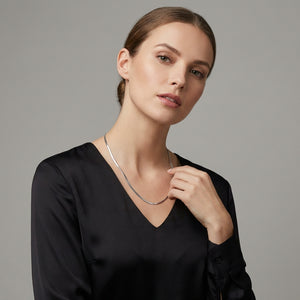 Woman in a black blouse with a silver necklace, looking slightly right against a gray background.
