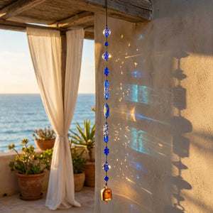 Blue glass wind chime casting colorful reflections on a sunny patio by the ocean.
