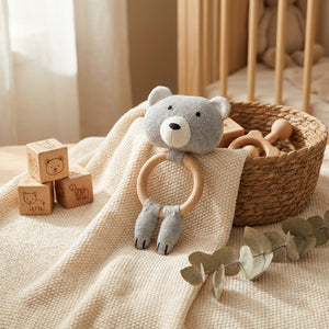 Gray bear rattle on beige blanket, with wooden blocks and basket in a softly lit, cozy room.