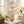 Colorful heart-shaped paper garland hanging in a sunlit room with flowers and wooden table.