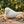 White ceramic bird with dotted lines, on a wooden surface with leaves and sticks, blurred greenery behind.