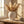White vase with pampas grass on wooden table, sunlit stone wall, window light streaming in.