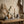 Vases with pampas and eucalyptus on a wooden tray beside a lit candle and ceramic cups on a bench.