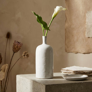 White calla lily in a sleek white vase on a stone surface, with beige textured background.