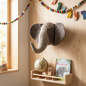 Elephant head decor on wooden wall, globe on shelf, colorful garlands, and toy blocks by window.