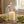 White candle under a glass dome on a wooden table, surrounded by green moss and smooth stones.
