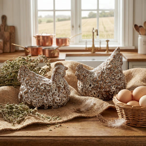 Ceramic chickens on burlap, basket of eggs, herbs, and copper pots by a window with countryside view.