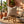 Striped pillow on wooden stool, surrounded by potted plants and books on a woven rug.