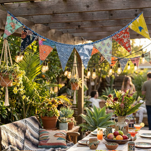 Colorful fabric bunting and string lights above a garden table with plants, fruits, and drinks.