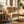 Cozy room with wooden furniture, fluffy beige throws, potted plants, and soft sunlight streaming in.