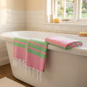 Pink and green striped towels on a white bathtub with a window and white tiled wall.