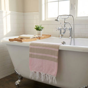 Clawfoot bathtub with pink towel, wooden tray, open book, plant, and chrome faucet under window.