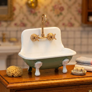 Miniature vintage sink with gold faucet, green basin, sponge, soap, and towels on wooden surface.