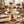 Two-tiered white cake with gold accents and berries on a wooden stand, set on a rustic table.