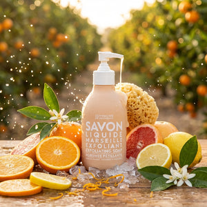 Soap bottle with citrus fruits, orange blossoms, and a sponge in an orchard setting.