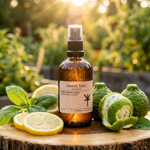 Brown glass spray bottle with lemons, basil, and bergamot on a wooden surface, sunlight in background.