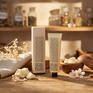 Hand cream tube and box on wood table with flowers and wooden bowl, warm sunlight ambiance.