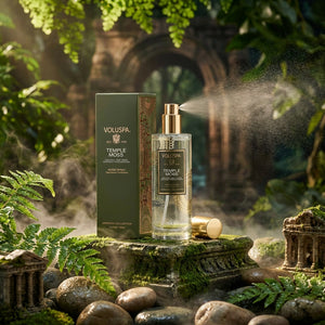Perfume bottle and box on mossy stones, surrounded by ferns and mist in a lush, green setting.