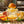 Orange juice splashes from a glass juicer, surrounded by sliced citrus fruits on a wooden table.