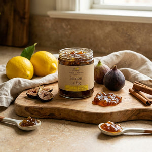Jar of lemon fig marmalade on a wooden board with figs, lemons, cinnamon, and spoons of marmalade.