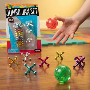Hand tossing a red ball among colorful jacks on wood floor, with jumbo jax set packaging in view.