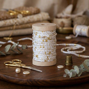 White and gold wired raffia ribbon with metallic thread on a wooden spool, ideal for holiday gift wrapping by CCOI.