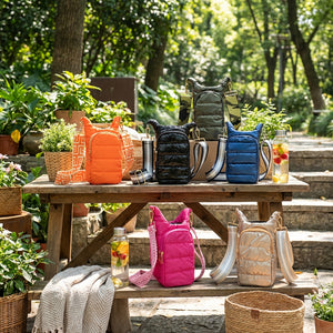 Colorful puffer bags on a wooden bench in a sunlit garden with lush green plants.