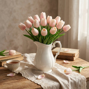 Pink tulips in a white vase on wooden table with lace cloth, books, and a teacup.