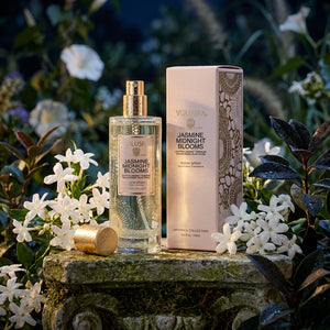 Perfume bottle and box on a stone ledge with white flowers and green foliage.