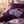 Lavender sleep mask on purple pillows, surrounded by lavender sprigs, petals, and a lit candle.