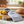 Wooden board with lemons, blueberries, striped towel, and crusty bread near copper pots and plants.