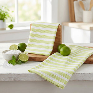 Green striped towels, limes, salt bowl, and mint on a white kitchen table with wooden accents.