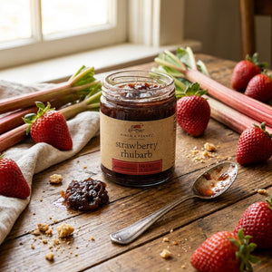 Jar of strawberry rhubarb preserve with scattered strawberries and rhubarb on a wooden table.