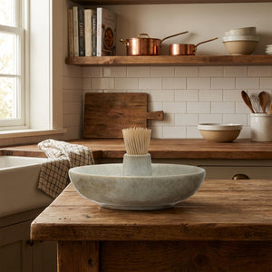 Ceramic dish with toothpicks on a wooden kitchen counter, with copper pots and a window.