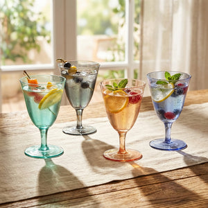 Four colorful goblets with fruit-infused drinks on a wooden table, sunlight streaming in.